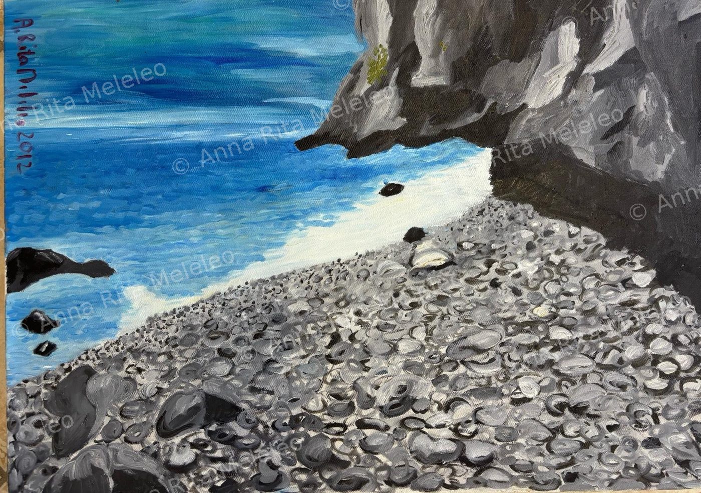 Spiaggia di ciottoli grigi dipinti uno a uno, mare azzurro e roccia a picco.